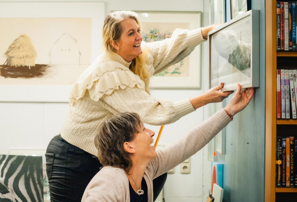 Vrijwilligers van de kringloopwinkel in Berkum hangen samen een schilderij op.